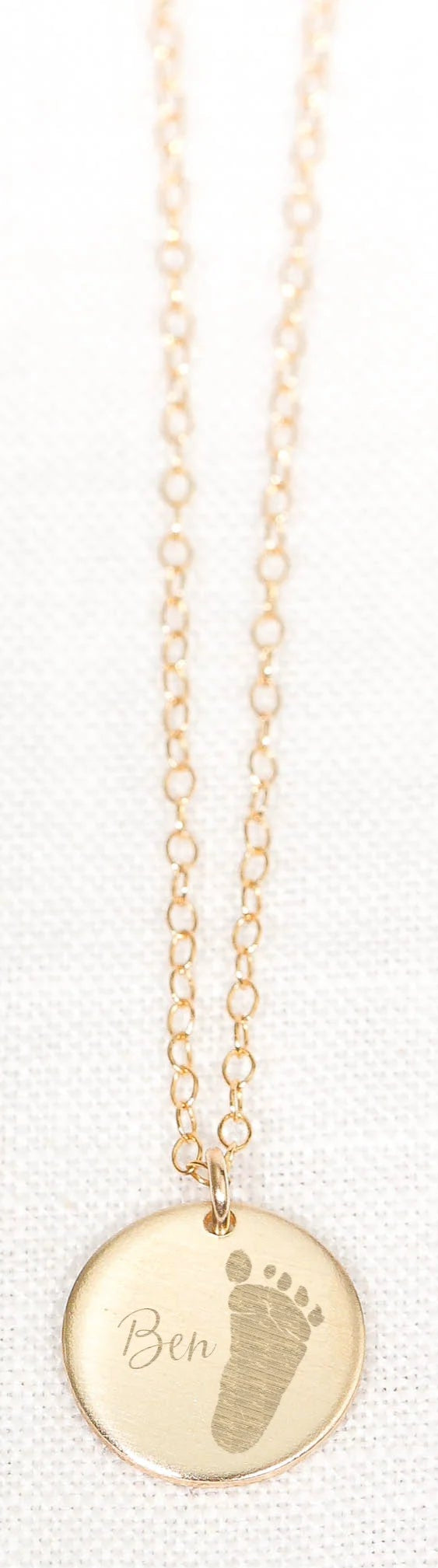 Gold necklace with a round pendant featuring a footprints design and the name.
