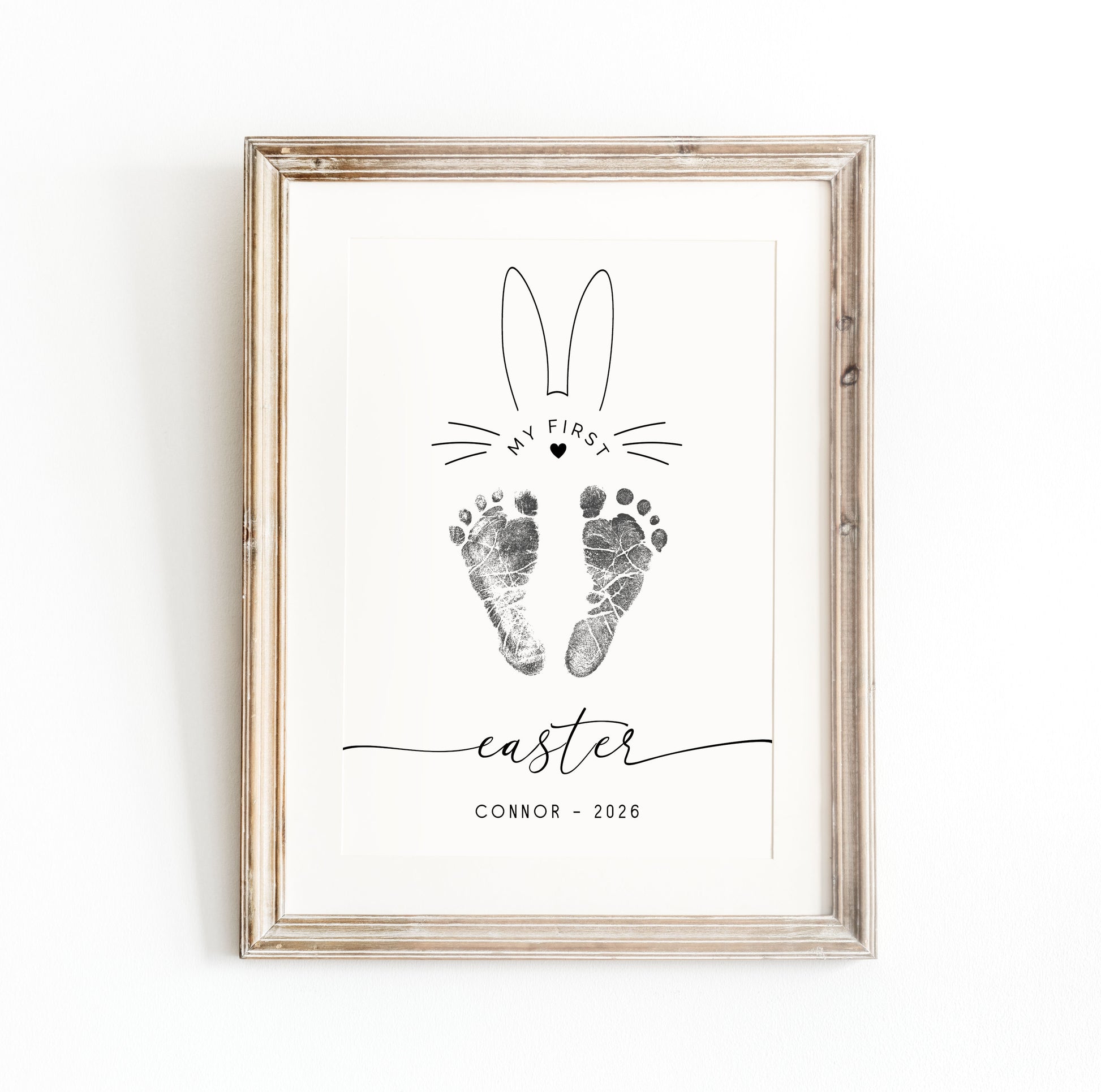 Framed print keepsake with bunny ears, baby footprints, and text on a white background