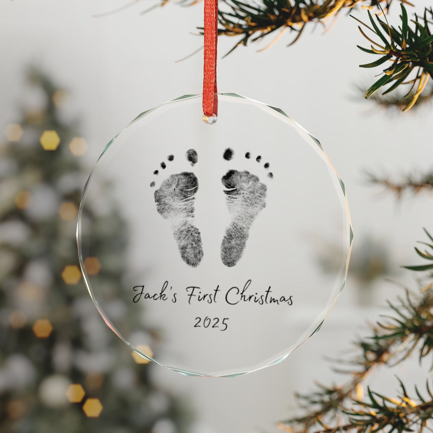 Custom glass ornament with footprints, First Christmas 2025' text, hanging on a tree branch.
