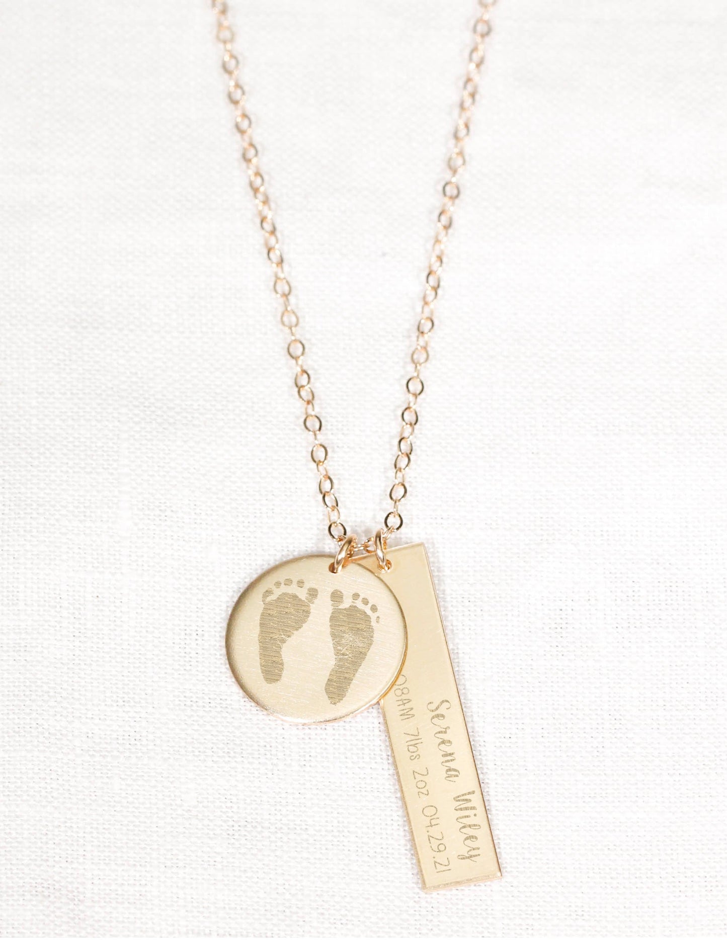 Gold necklace with footprints and text on a white background
