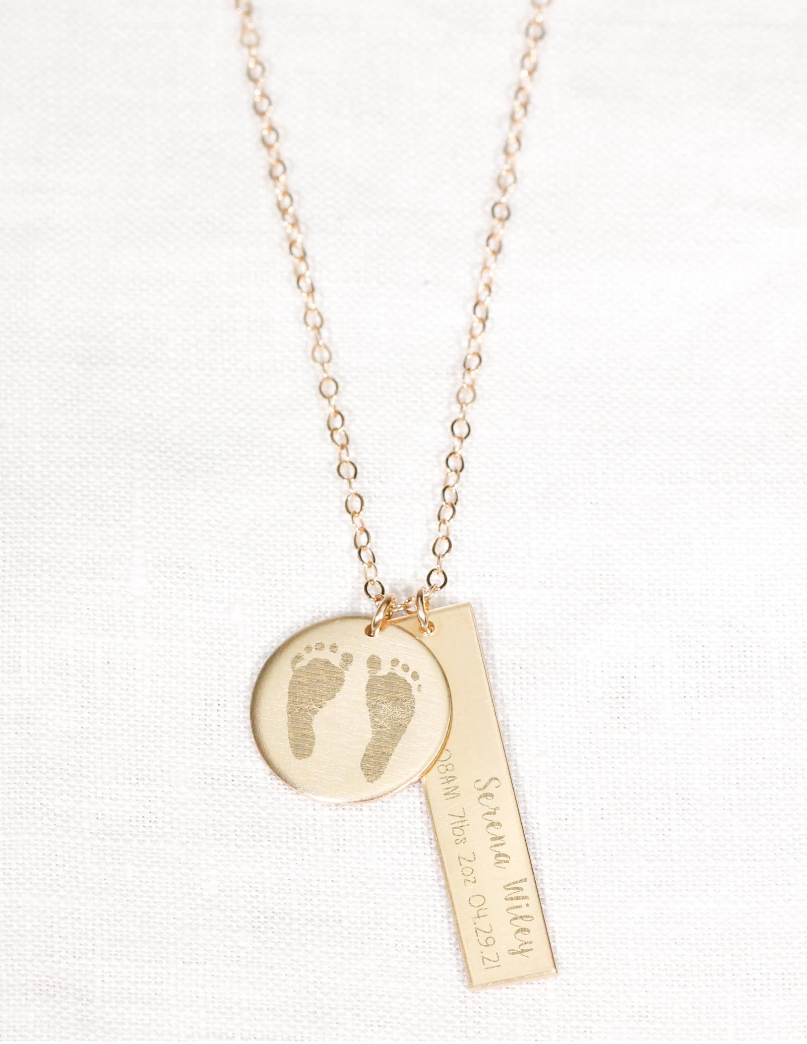 Gold necklace with footprints and text on a white background