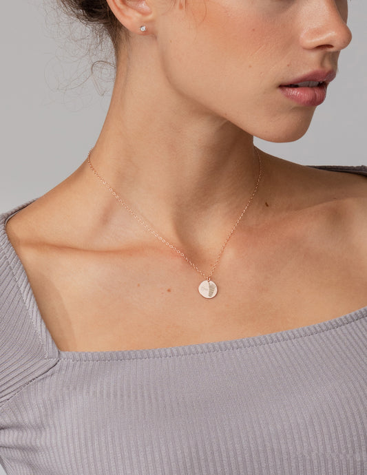 Close-up of a person wearing a delicate gold necklace with a small round pendant on a neutral background.