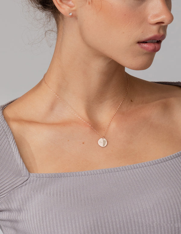 Close-up of a person wearing a delicate gold necklace with a small round pendant on a neutral background.